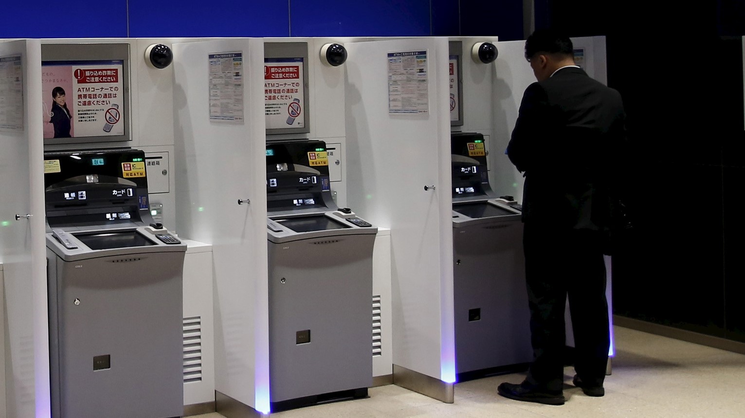 Man stands in front of an ATM of Mizuho Financial Group's Mizuho bank